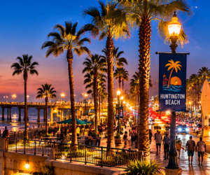 Nighttime panoramic view of Huntington Beach Pier, illuminated Main Street, palm-lined coastal streets, and Pacific Ocean in Huntington Beach, Orange County, California.