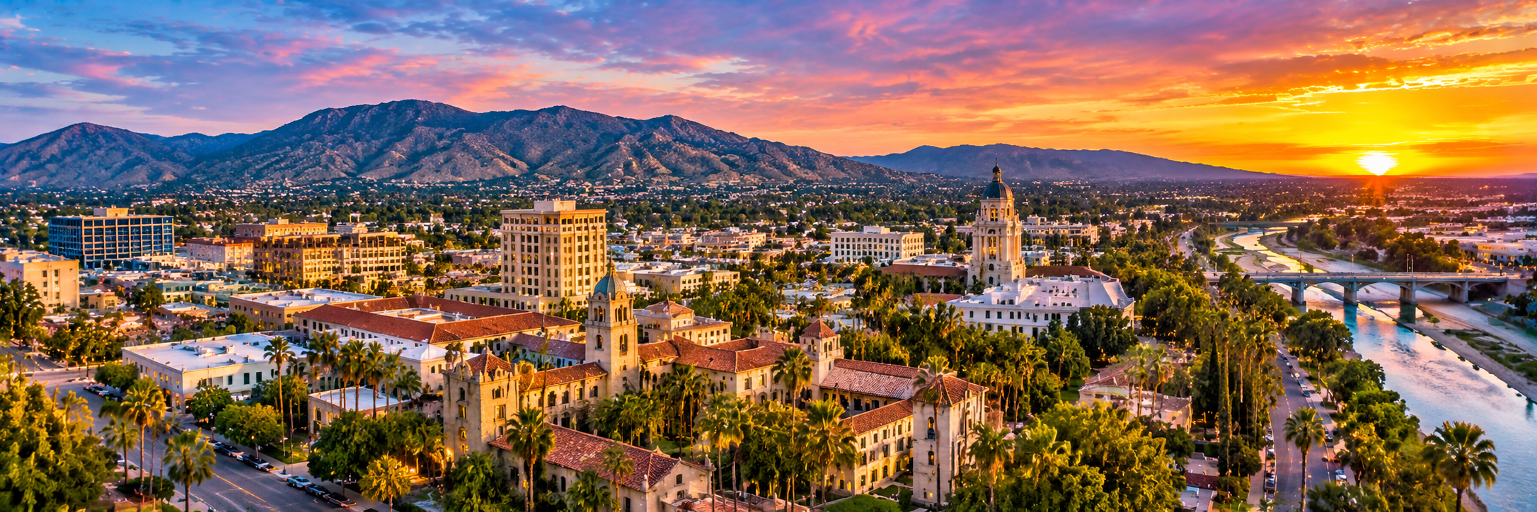 Aerial panoramic view of Downtown Riverside, historic Mission Inn, Riverside County Courthouse, Santa Ana River, and surrounding mountains at sunset in Riverside, California.