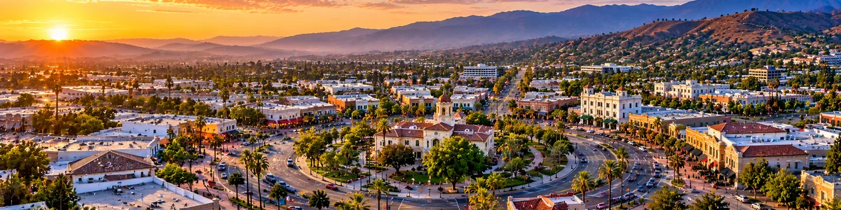 Aerial panoramic illustration of Downtown Corona, historic Grand Boulevard district, palm-lined streets, and surrounding hills at sunrise in Corona, California.