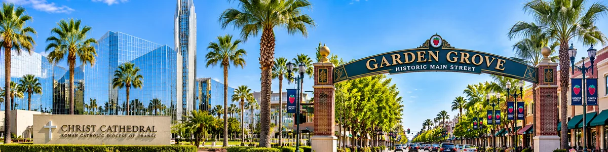 Bright daytime panoramic view of Christ Cathedral, Historic Main Street, palm-lined streets and commercial buildings in Garden Grove, Orange County, California.
